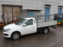 Белый грузовой автомобиль ВИС с установленным металлическим каркасом, вид сбоку на фоне производственного здания