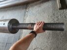 Металлическая тяга с нарезанной крупной резьбой для соединения элементов пристёжки крепления башенного крана, держит человек в цеху
