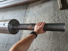 Металлическая тяга с нарезанной крупной резьбой для соединения элементов пристёжки крепления башенного крана, держит человек в цеху