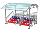 3D-визуализация готовой трибуны с навесом из прозрачного поликарбоната, установлены пластиковые сиденья красного и синего цвета, вид в полный рост