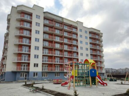 Жилой комплекс „Самолет“ в Крымске: фасад здания с установленными белыми металлическими ограждениями балконов и детской игровой площадкой